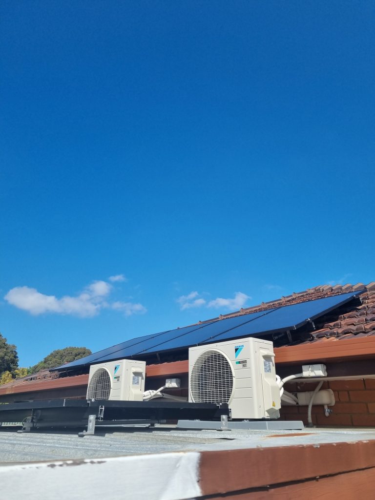 A rooftop with solar panels and two air-conditioner compressor units on adjacent roof.