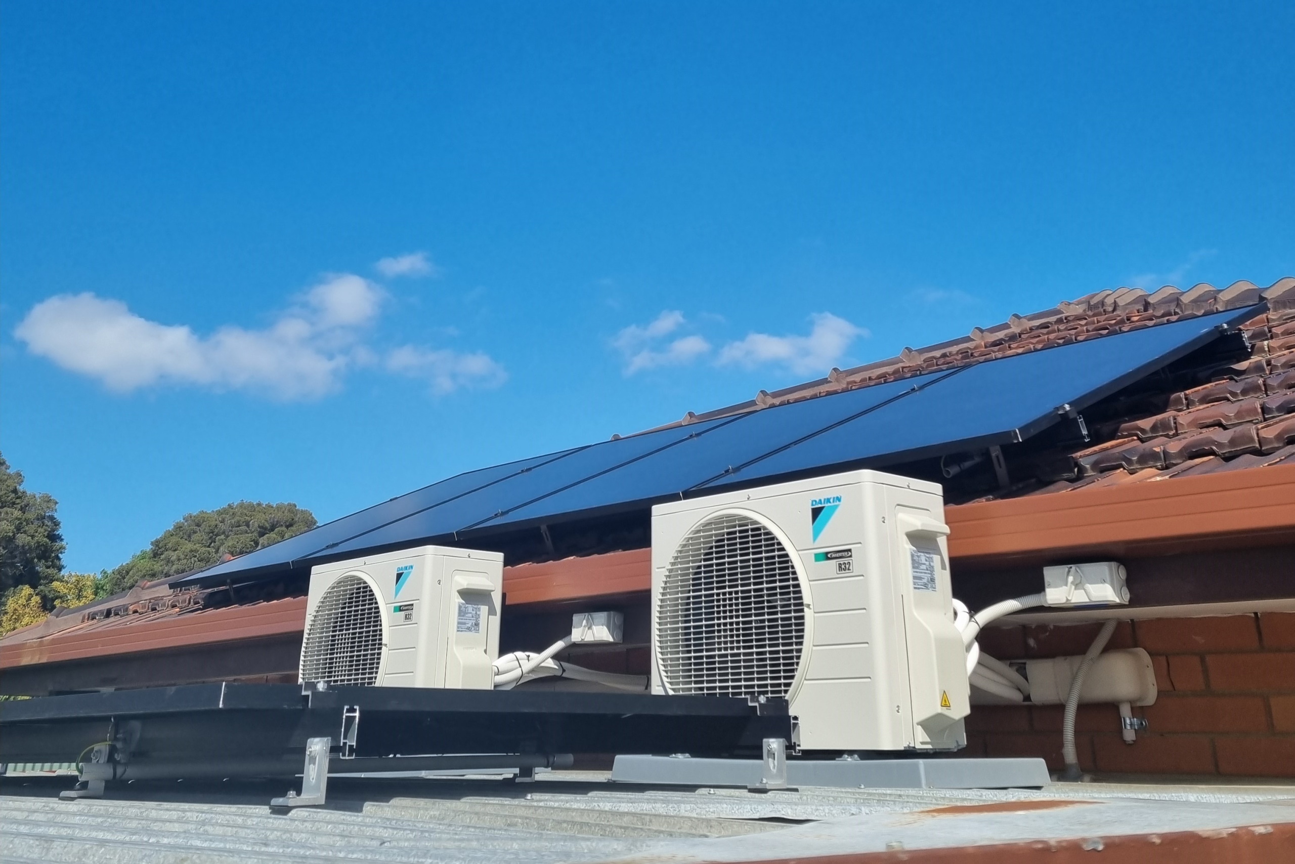 A rooftop with solar panels and two air-conditioner compressor units on adjacent roof.
